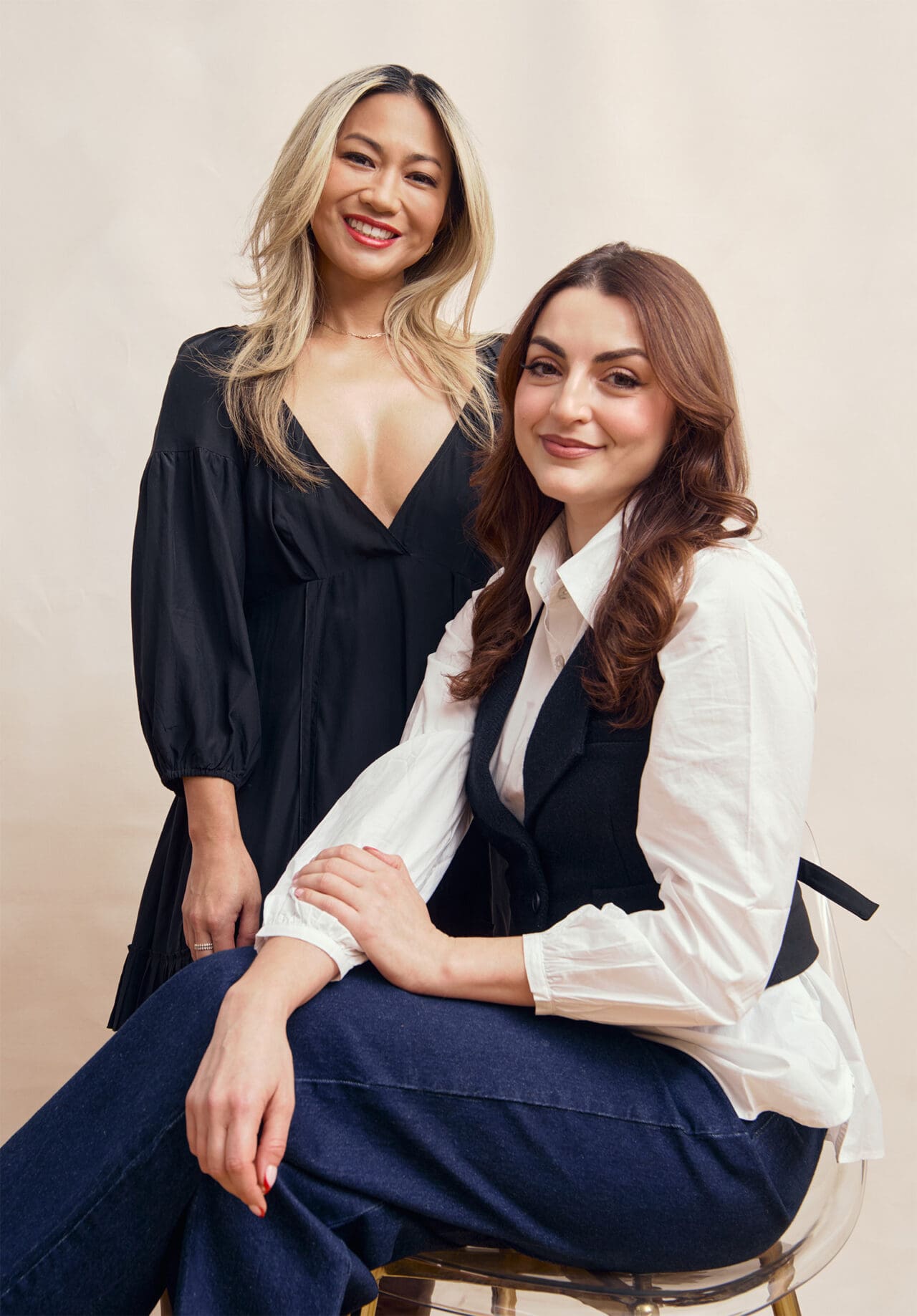 Joyce de Lemos and Charlotte Palermino, Co-Founders of Dieux Skin, seated on a chair, dressed in black and white tops