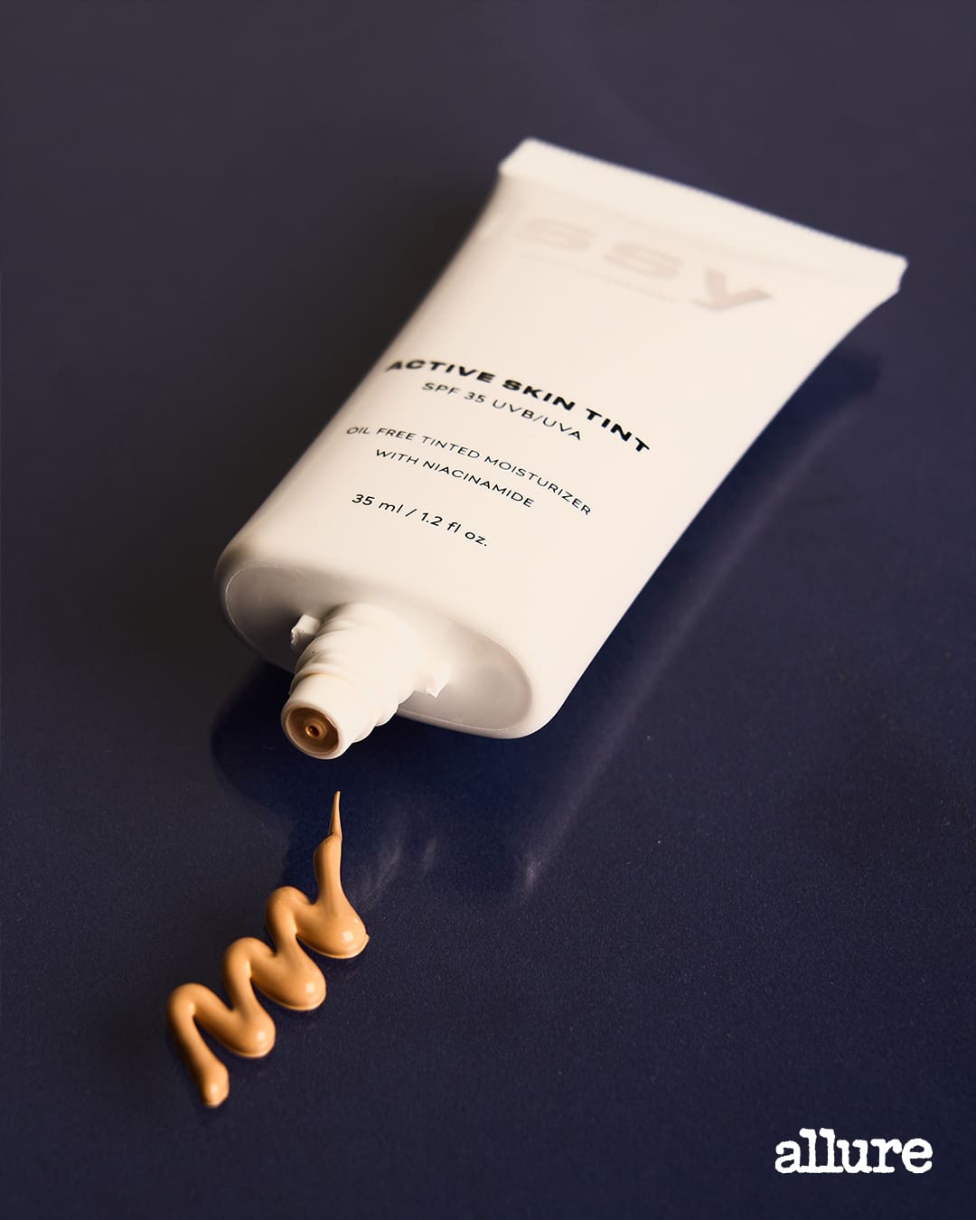 A tube of the Issy Active Skin Tint foundation placed on a blue table next to a swatch of the product.