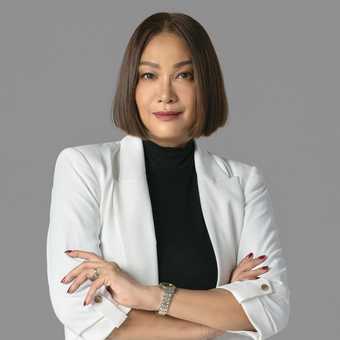 Professional woman with a sleek bob in a white blazer and black top, arms crossed against a gray background.