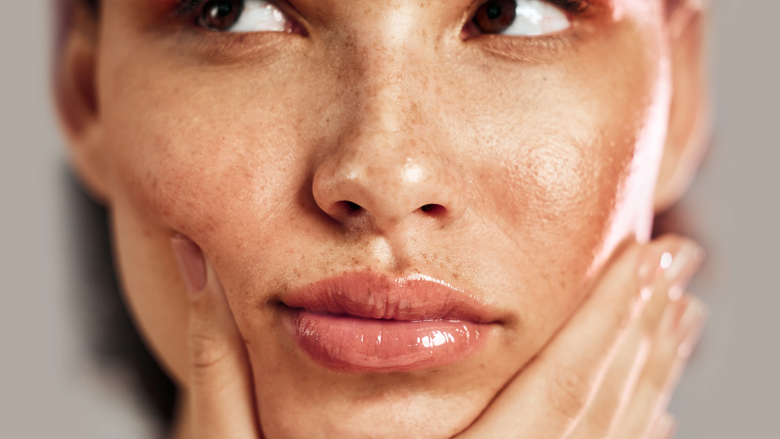 Close-up of a woman's freckled face, showing nose, lips, and cheek with glossy lips and smooth skin texture.