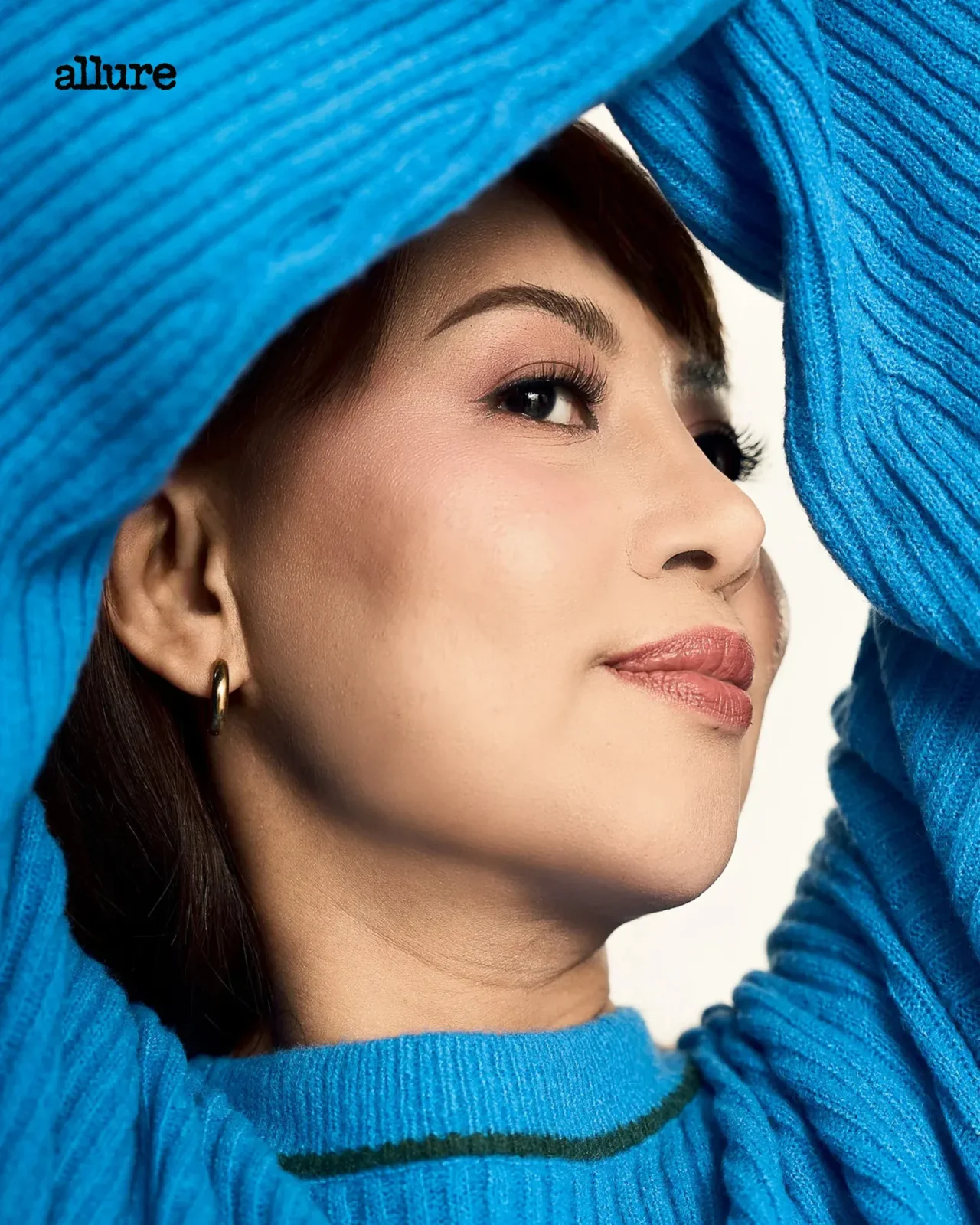 Close-up portrait of a woman with a bright blue knit scarf framing her face; Allure logo in the top-left corner.