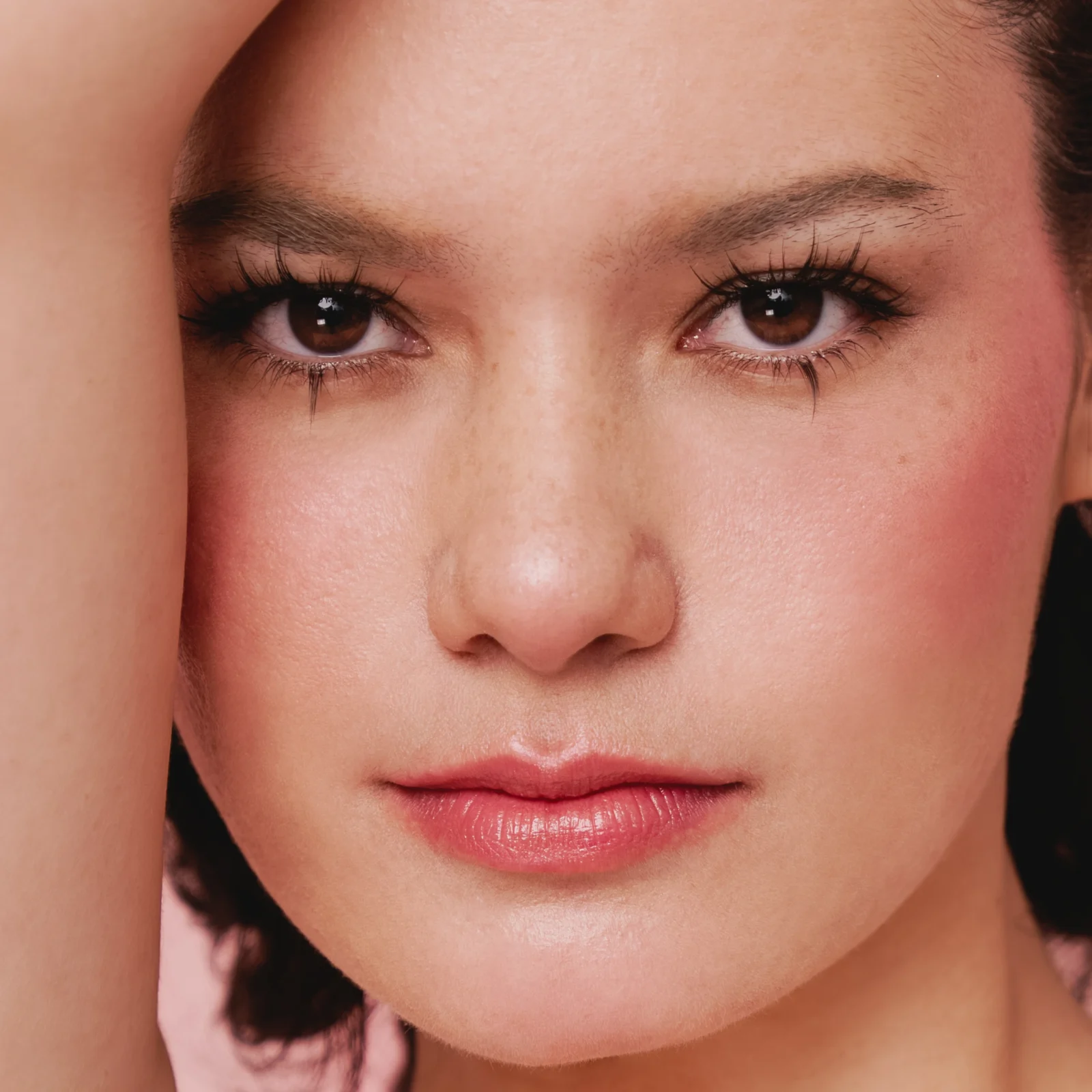 Close-up of a young woman's face with smooth skin, brown eyes, and pink lips, looking softly at the camera.