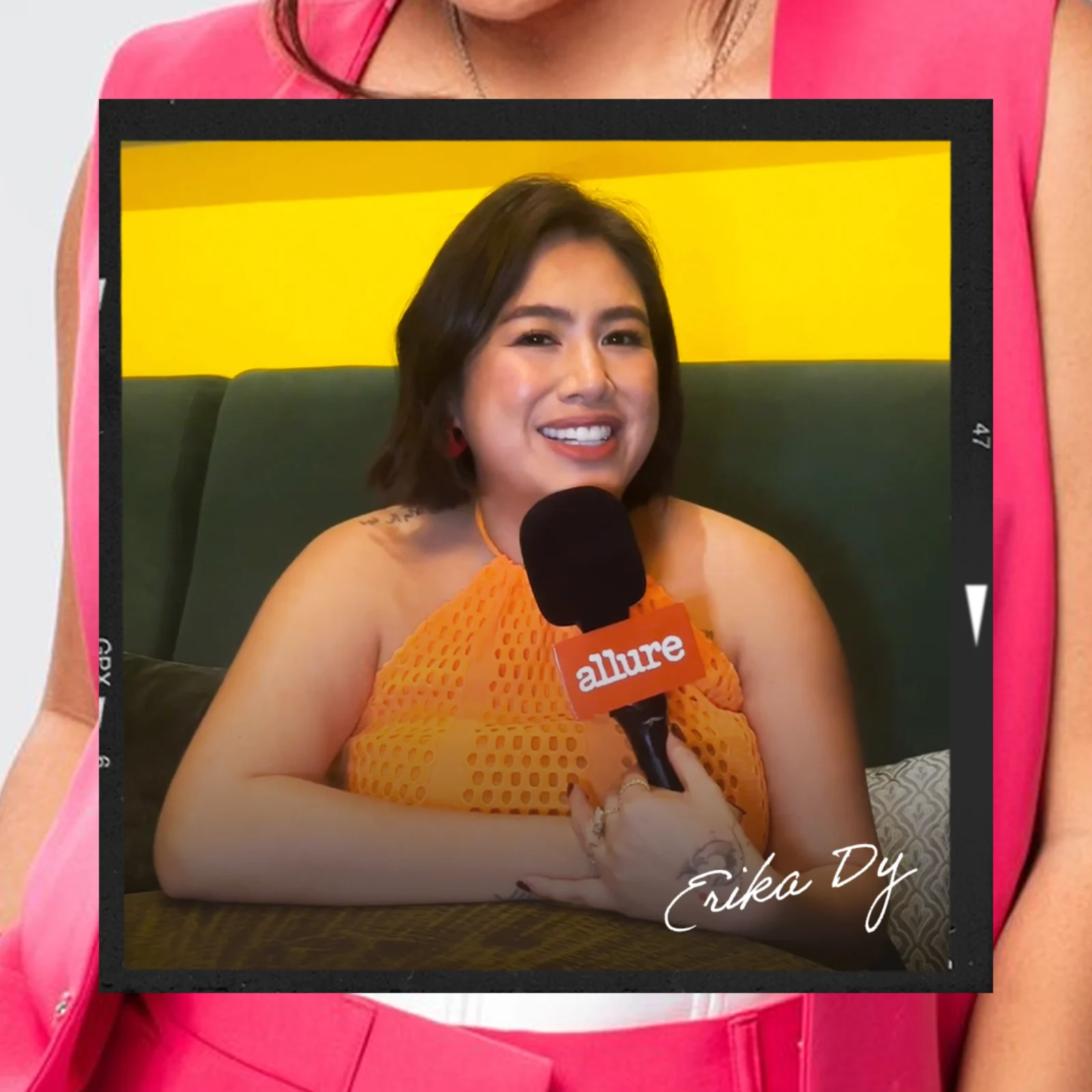 Smiling woman in an orange top holds a black microphone labeled Allure during an interview.