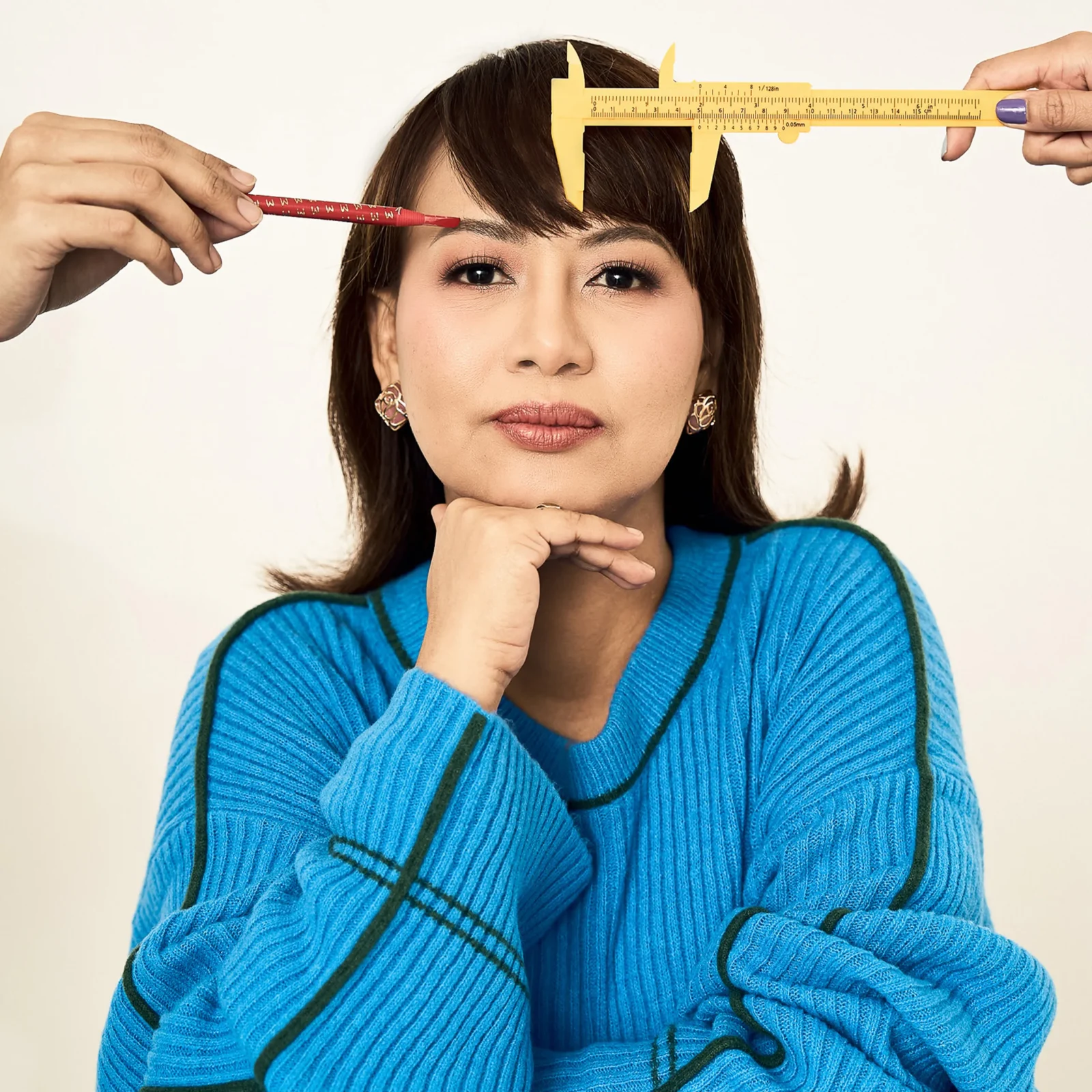 Close-up of a woman’s face while a yellow caliper spans her forehead and a red pencil points at her eyebrow for measurement.