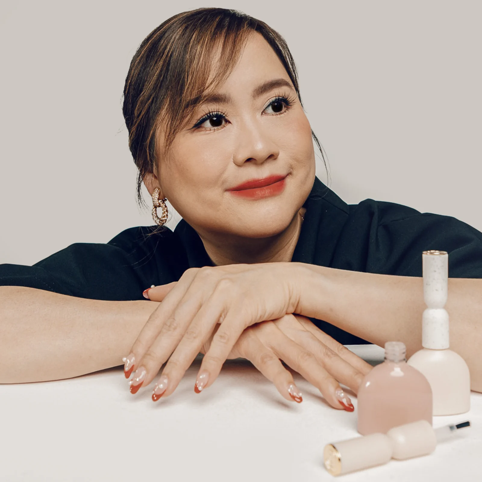 Close-up of a woman's hands with red-and-white nail art resting on a table, with nail polish bottles nearby.
