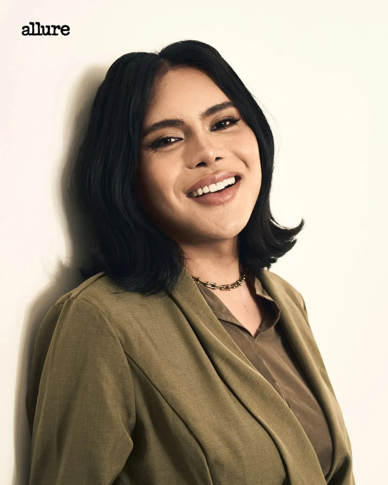 Smiling woman with shoulder-length dark hair in an olive blazer against a light background; Allure logo visible in the top-left corner.