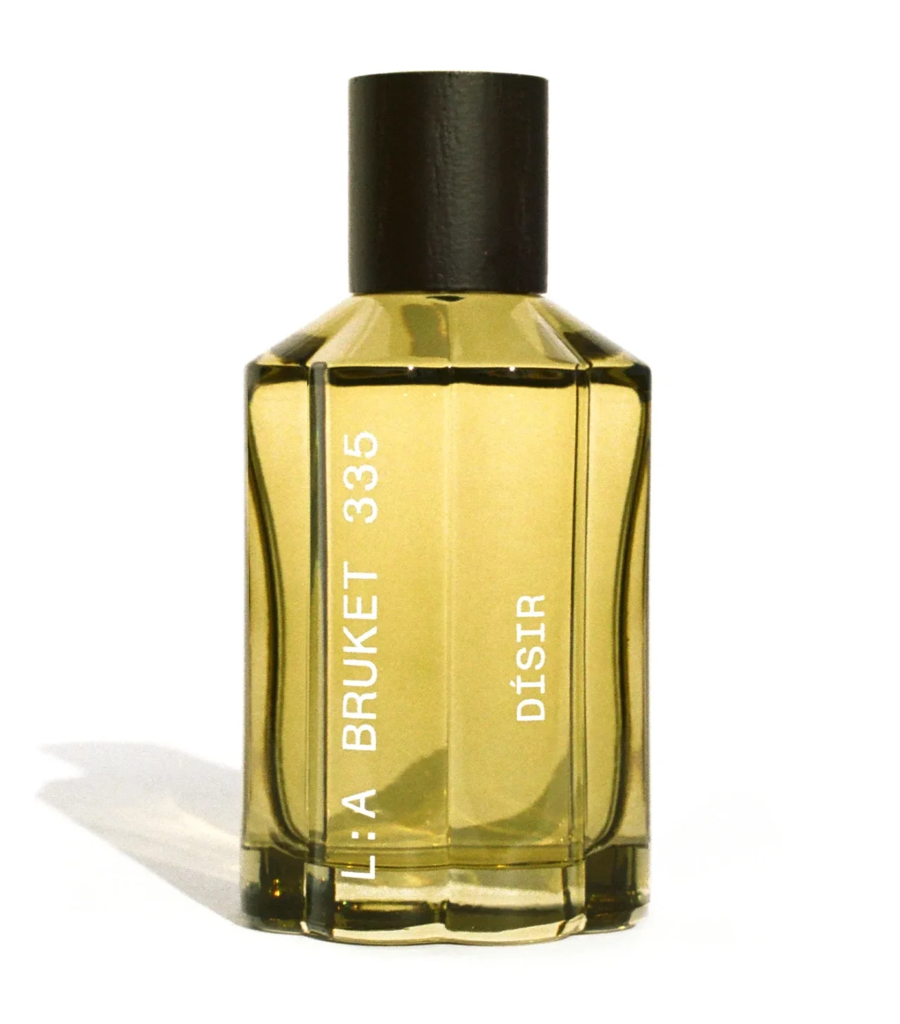 Gold-toned glass perfume bottle with a black cap, standing upright on a white surface.