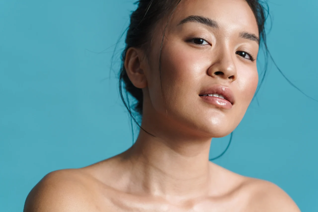 Close-up portrait of a woman’s lower face and neck against a blue background, showcasing smooth skin and subtle makeup.