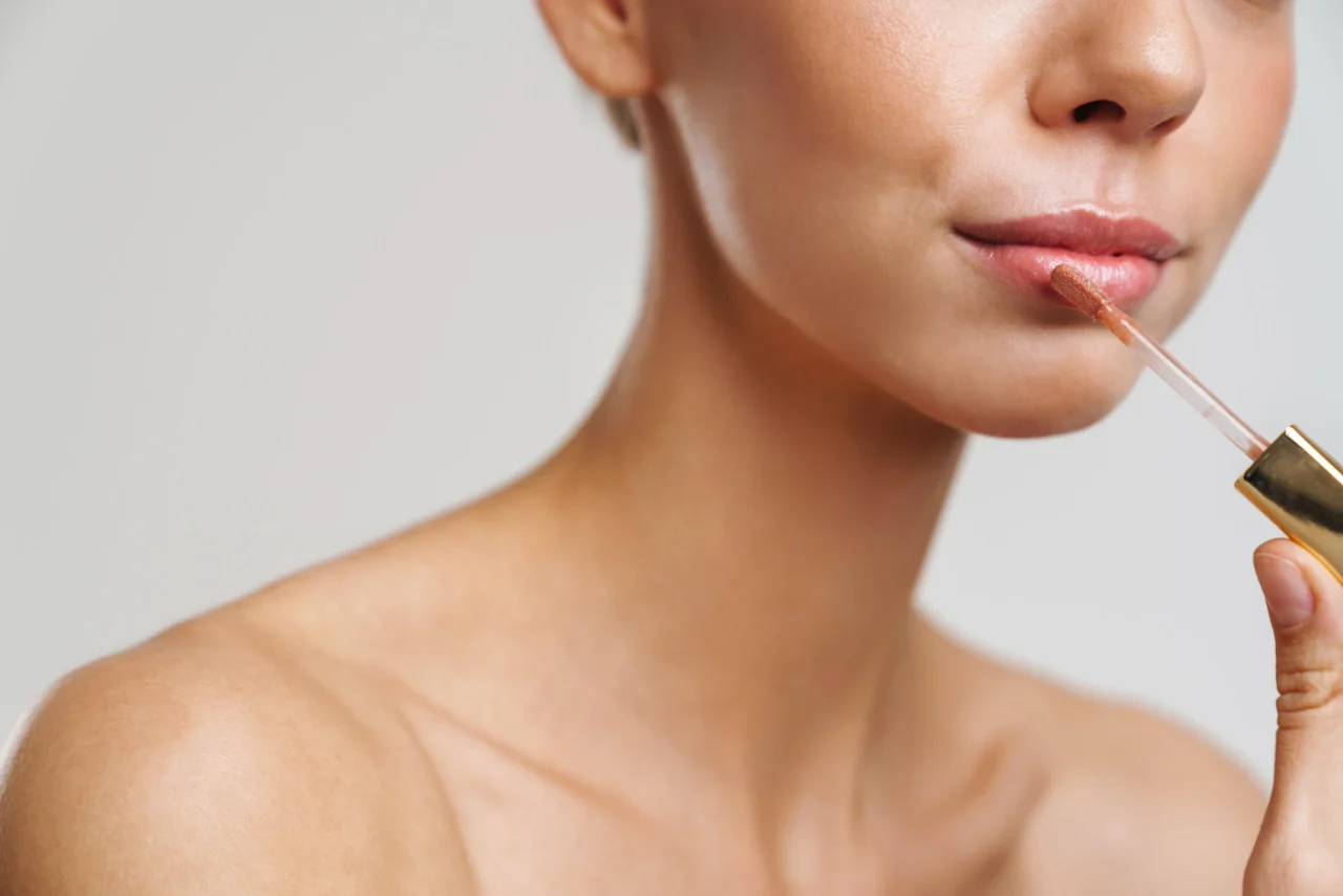 Close-up of a person applying nude lip gloss with a doe-foot wand near the lips.
