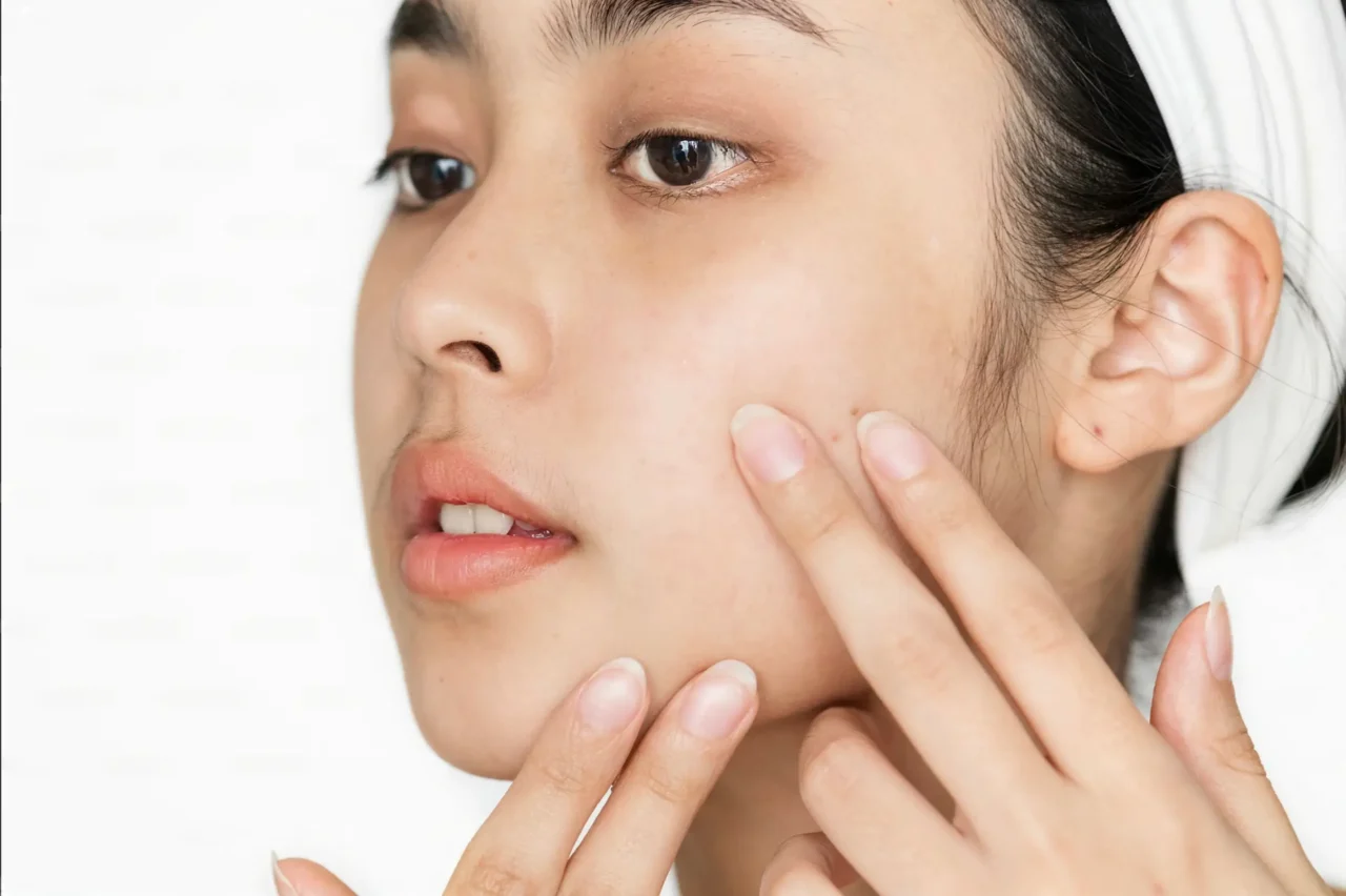 Close-up of a woman's face with hands touching her cheek, showing smooth skin and a calm expression (skincare context).
