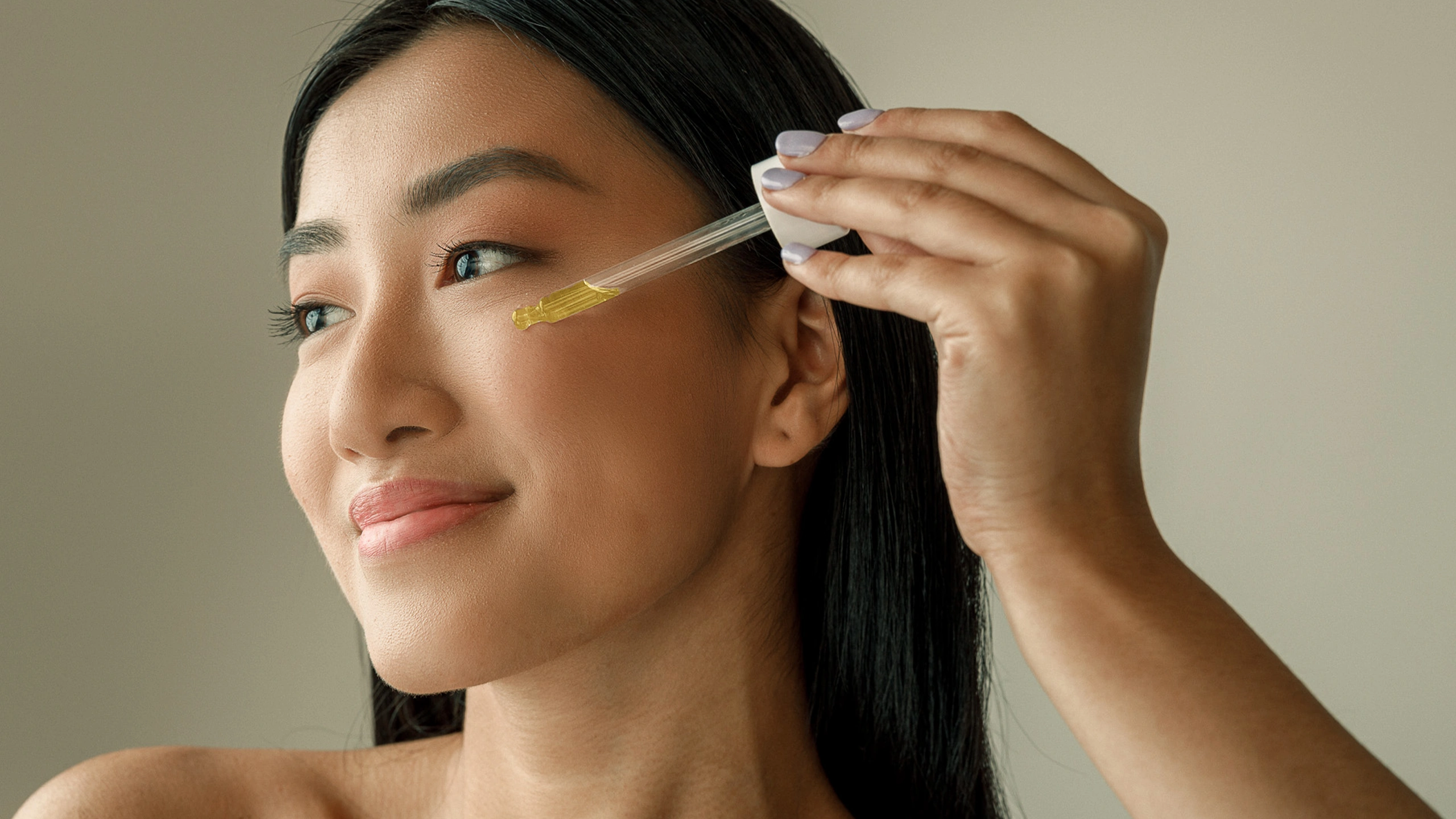 Woman applying facial serum under her eye with a dropper near her temple, close-up skincare moment