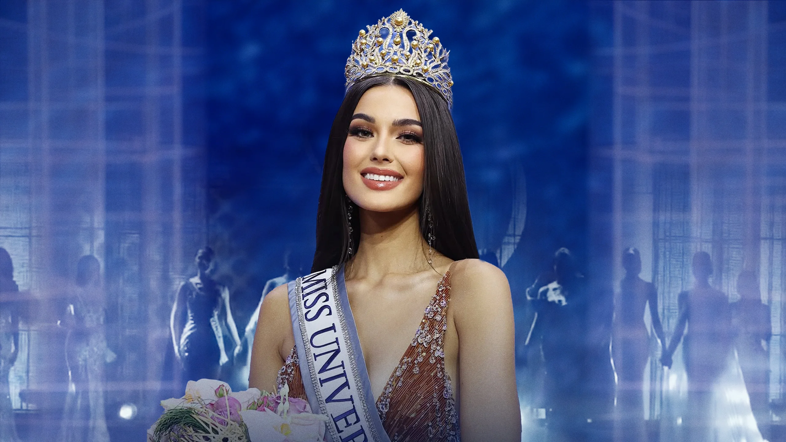 Miss Universe contestant wearing a jeweled crown and sash, holding a bouquet on a blue-lit stage, smiling at the camera.
