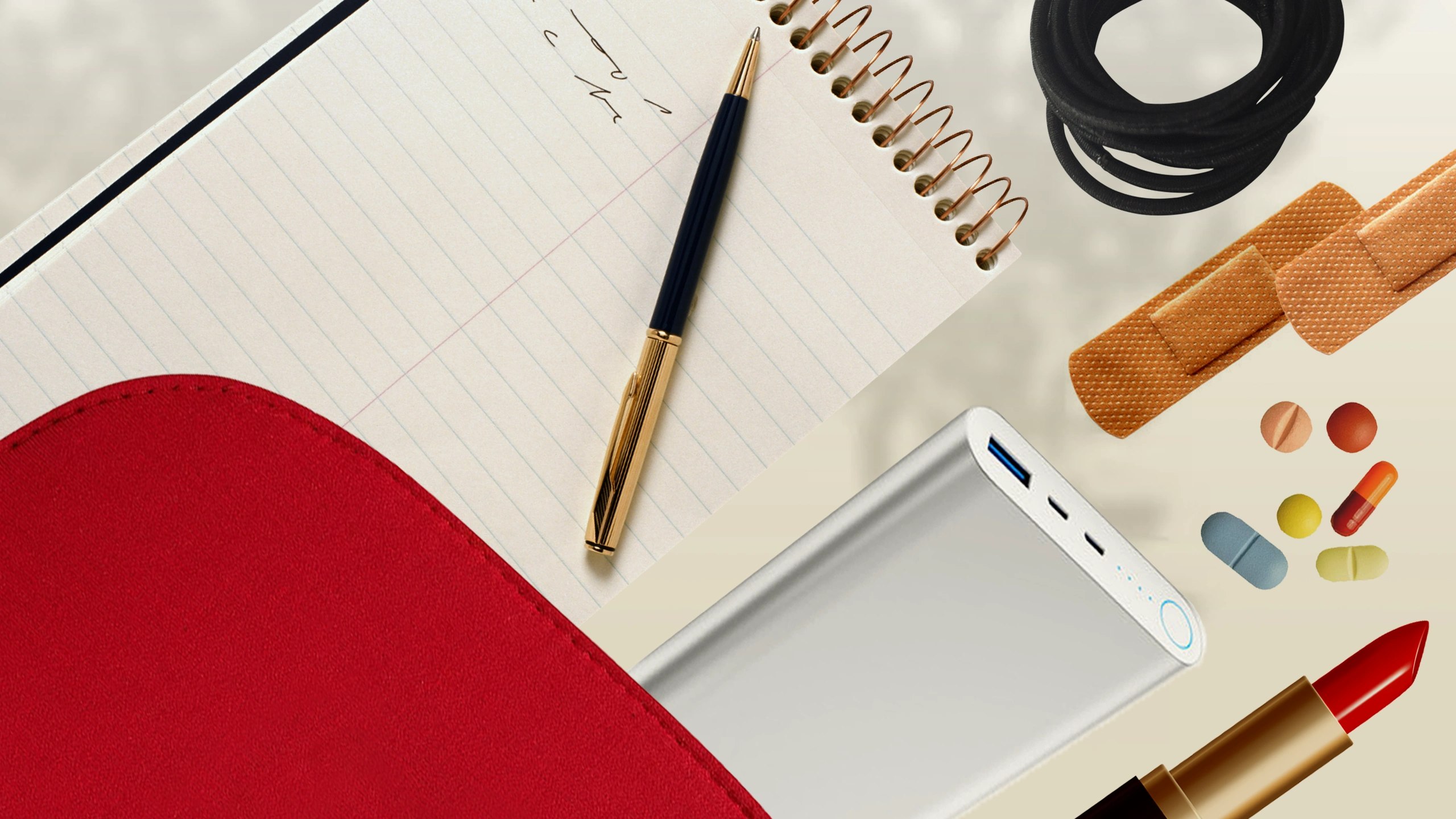 Flat lay of office supplies on a beige background: spiral notebook, gold-and-black pen, red notebook cover, USB power bank, black cord, orange adhesive bandages, scattered capsules, and red lipstick nearby.
