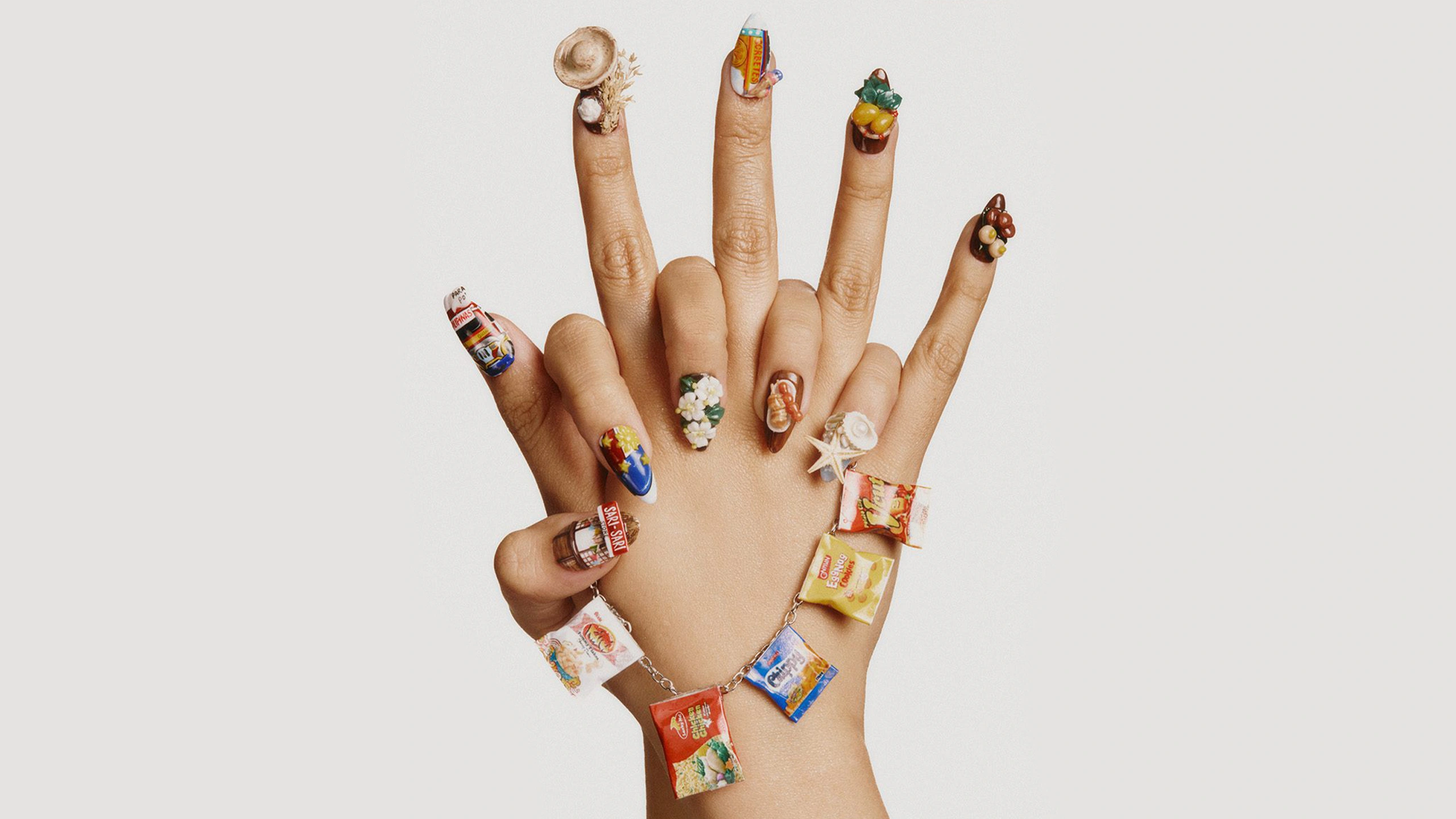 Hands showing candy-themed nail art with miniature treats on each finger and candy-wrap bracelets.