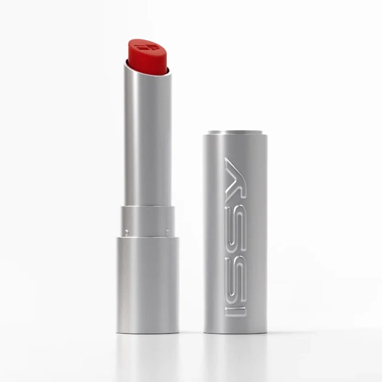Red lipstick in a metallic silver tube, cap removed and standing upright on a white surface.