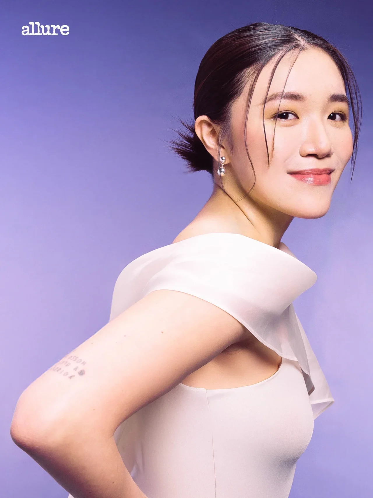 Portrait of a woman in a pale pink dress, facing slightly away, with an Allure logo in the top left against a lavender backdrop.