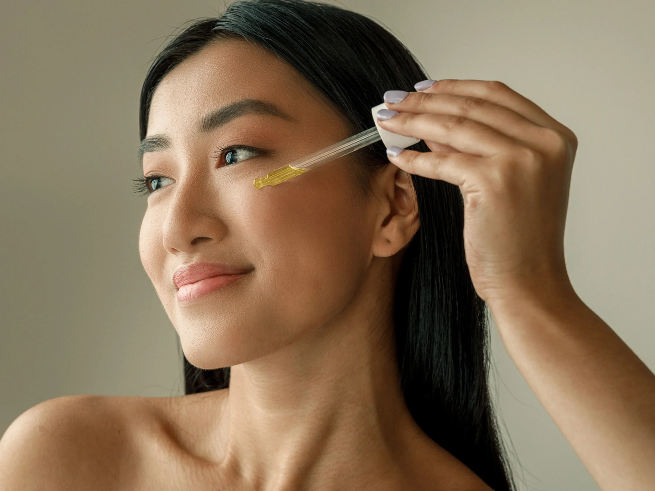 Close-up of a woman applying skincare serum to her temple with a dropper