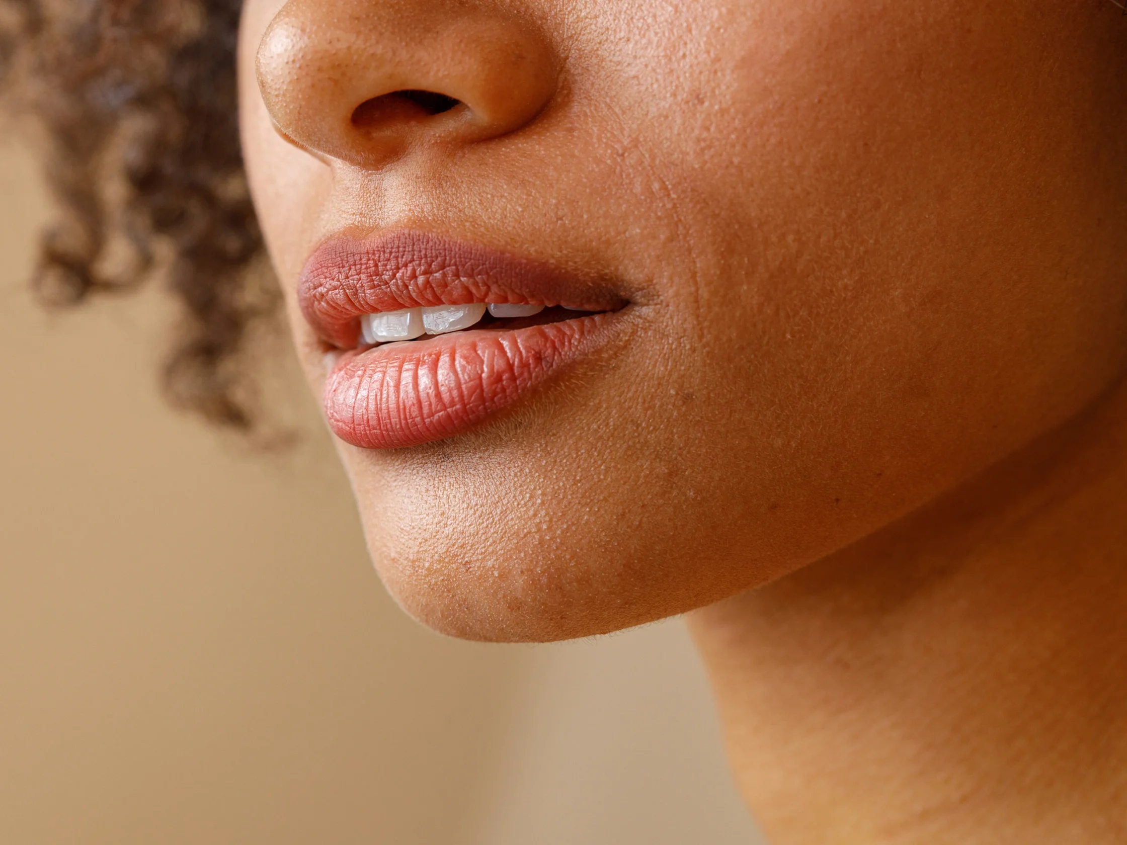 Close-up of a person's lips and lower nose, with visible skin texture and a hint of teeth as the lips part slightly.