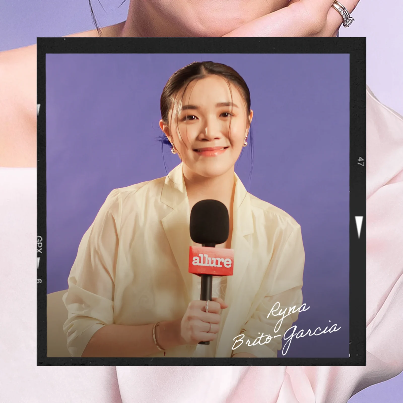 Woman wearing a light blouse holds a microphone with the red 'Allure' logo, as if giving an interview or hosting a segment.