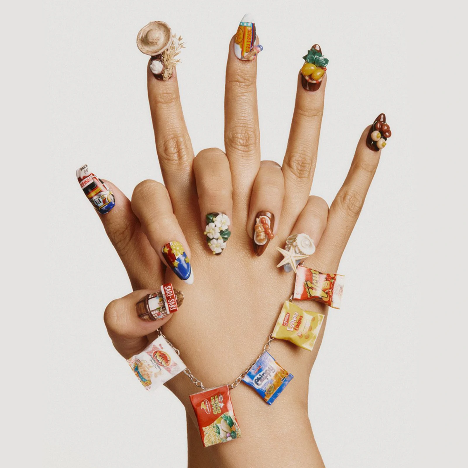 Close-up of a hand with fingernails covered in small colorful candy wrappers as nail art showcase, against a light background.