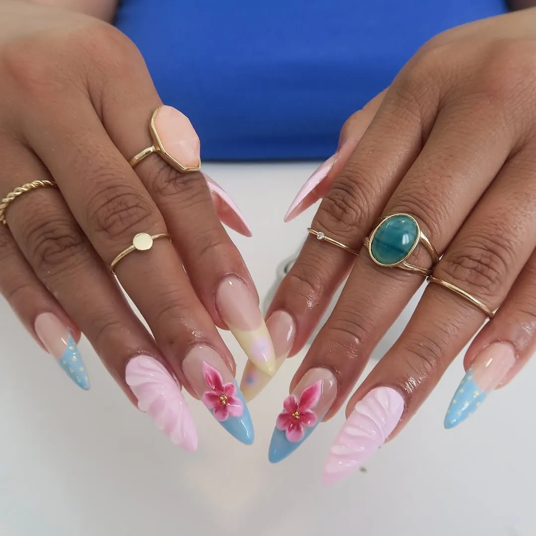 Hands with long pastel gradient nail art featuring pink and blue tips and gold rings on fingers.