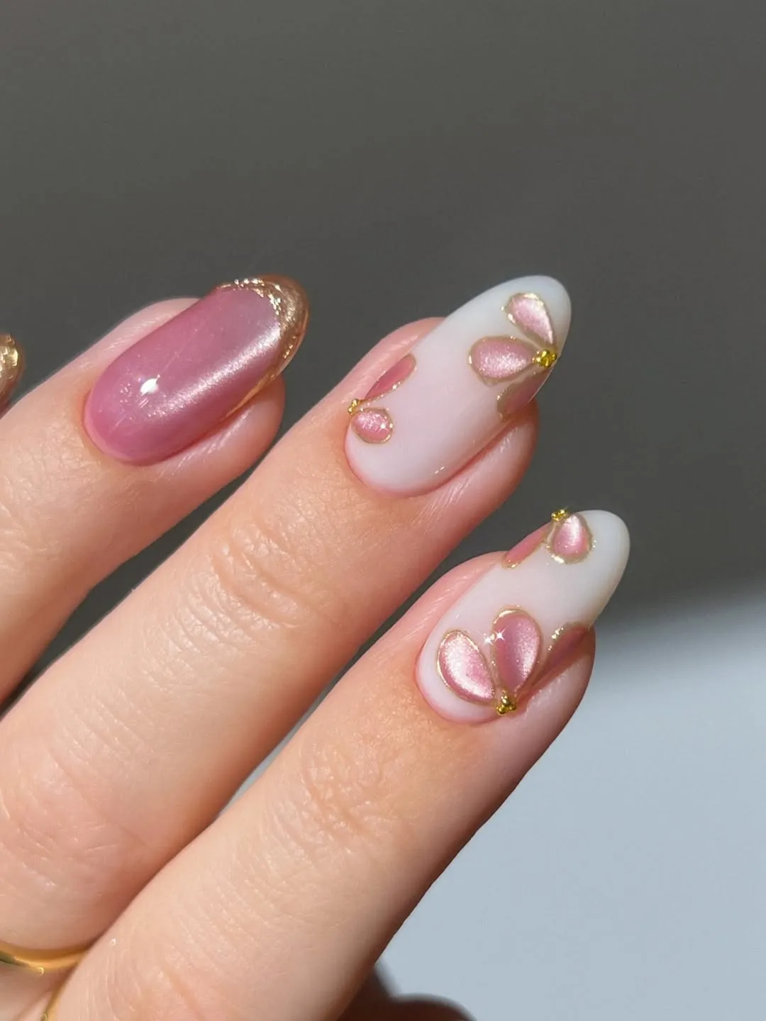 Close-up of manicured nails with a pale pink base and gold-edged pink petal designs on the index and ring fingers.