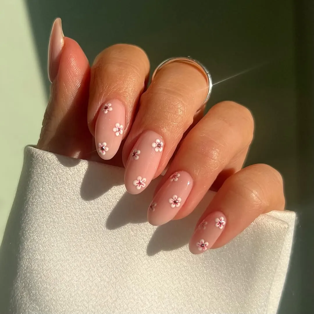 Close-up of pale pink manicured nails with small white flower embellishments on each nail.