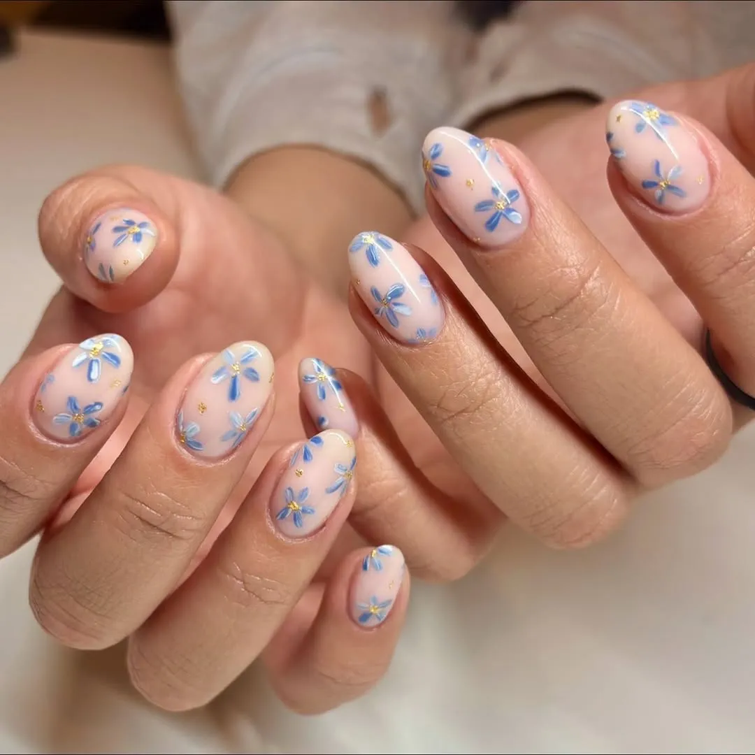 Nails with pale pink base and blue floral nail art, small yellow centers.