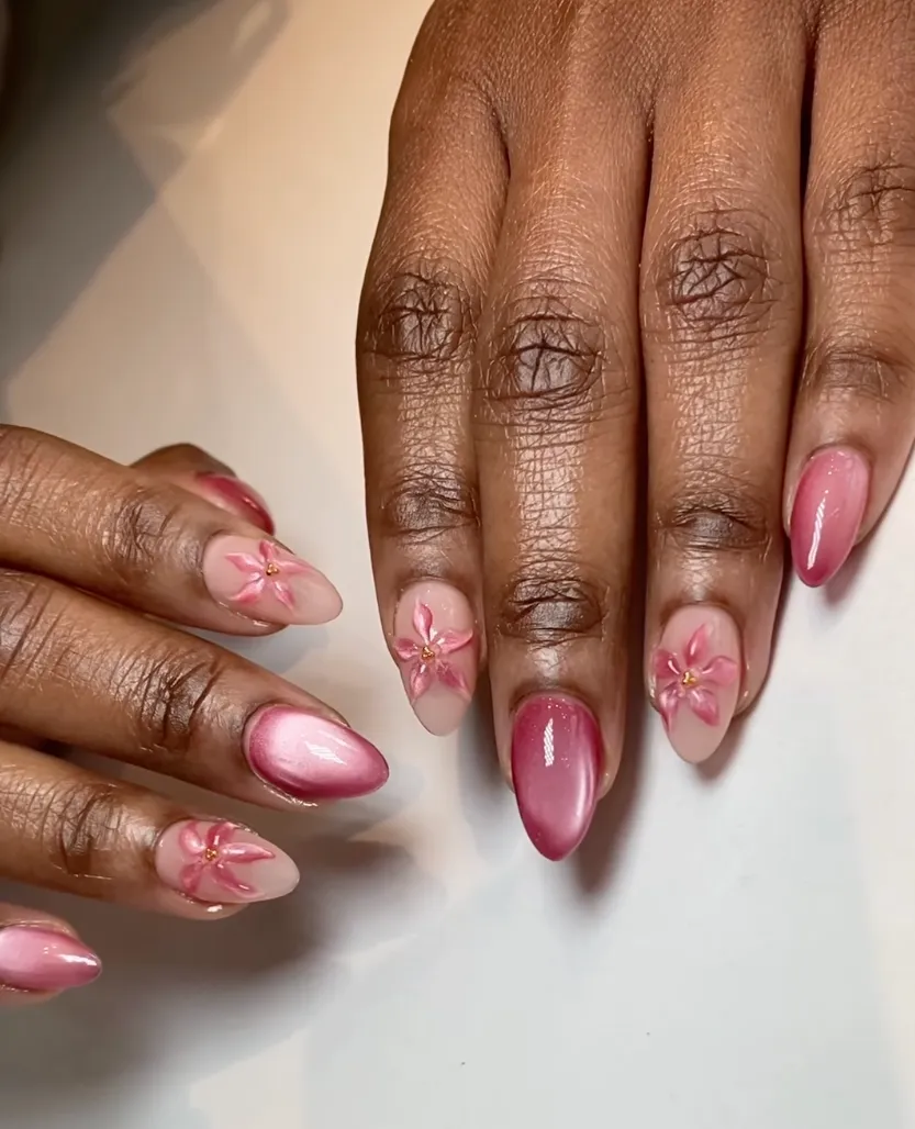 Manicured hands with pink gradient nails; several nails feature delicate pink flower decals on a nude base.