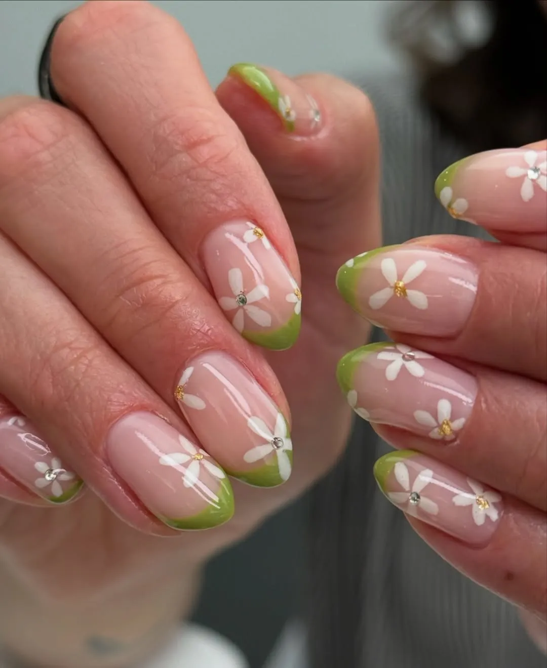 Nail manicure with pink base and lime green French tips decorated with white daisy flowers and small gem centers