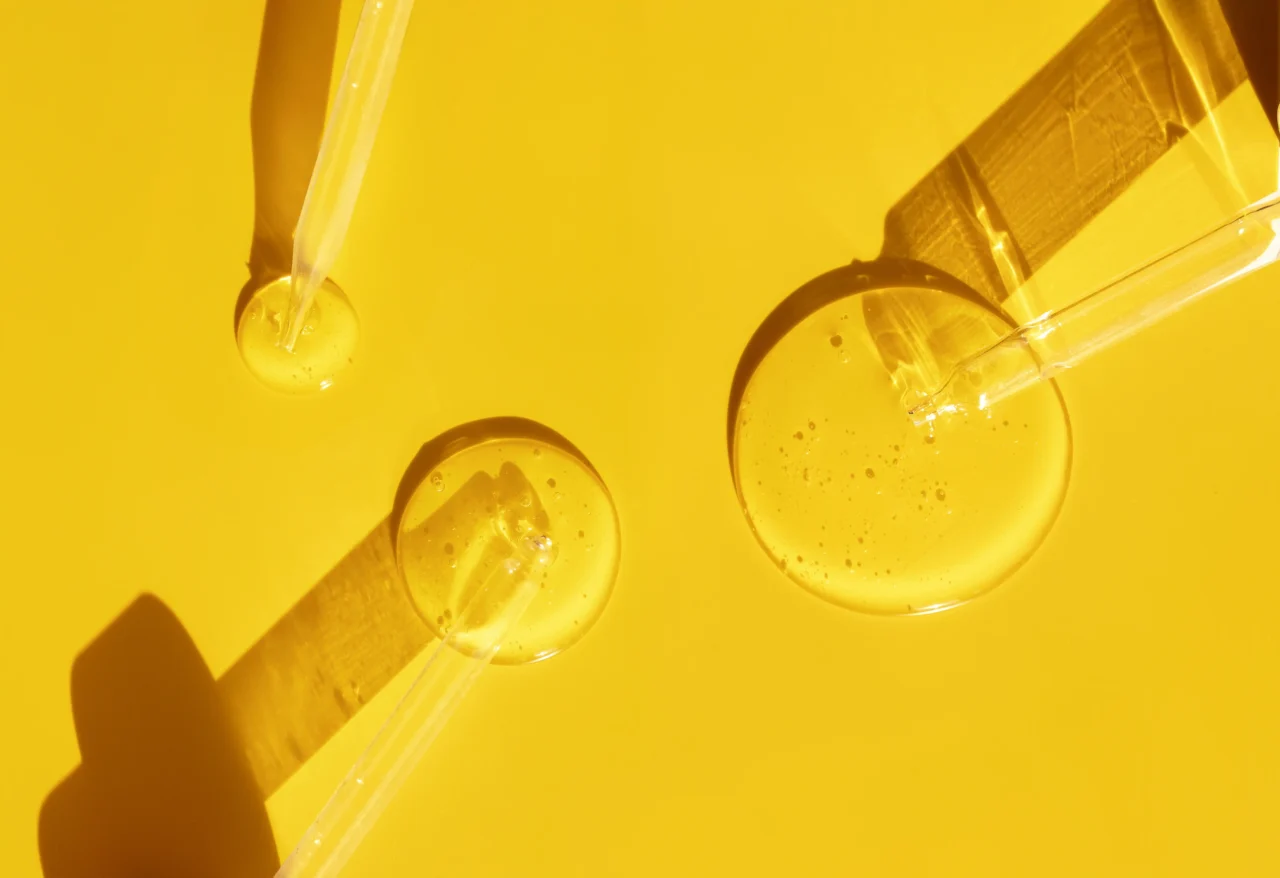 Pipette dispensing liquid into a petri dish on a wooden tray with a yellow backdrop, laboratory setting