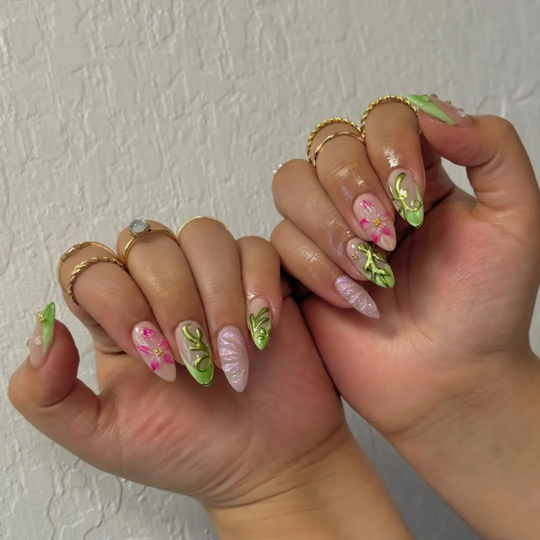 Nail art on both hands with green-tipped almond nails, pink floral accents, and gold rings on the fingers.