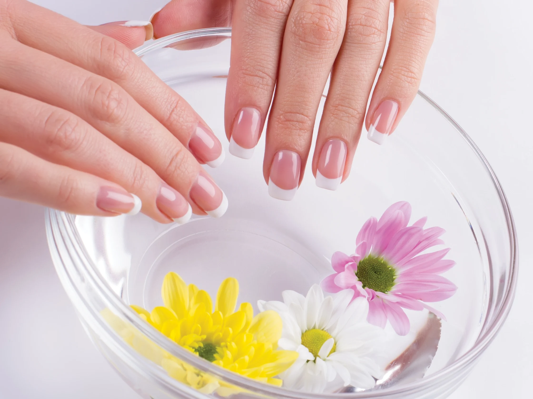 Close-up of hands with French-manicured nails arranging yellow and pink flowers in a glass bowl