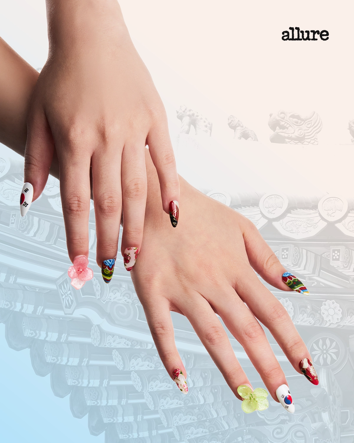 Close-up of hands with long, decorated acrylic nails resting above a pale, decorative background; Allure logo in the corner.