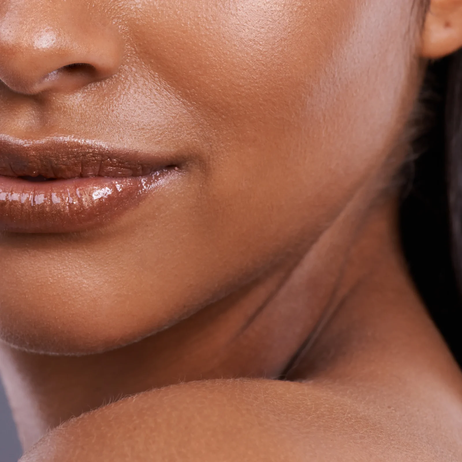 Close-up of a brown-skinned mouth area, with slightly parted glossy lips and visible skin texture around the chin and nose.