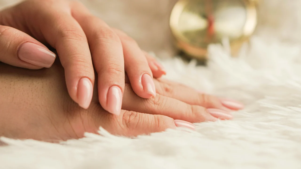 Close-up of a hand with pale pink manicured nails resting on a fluffy white surface.