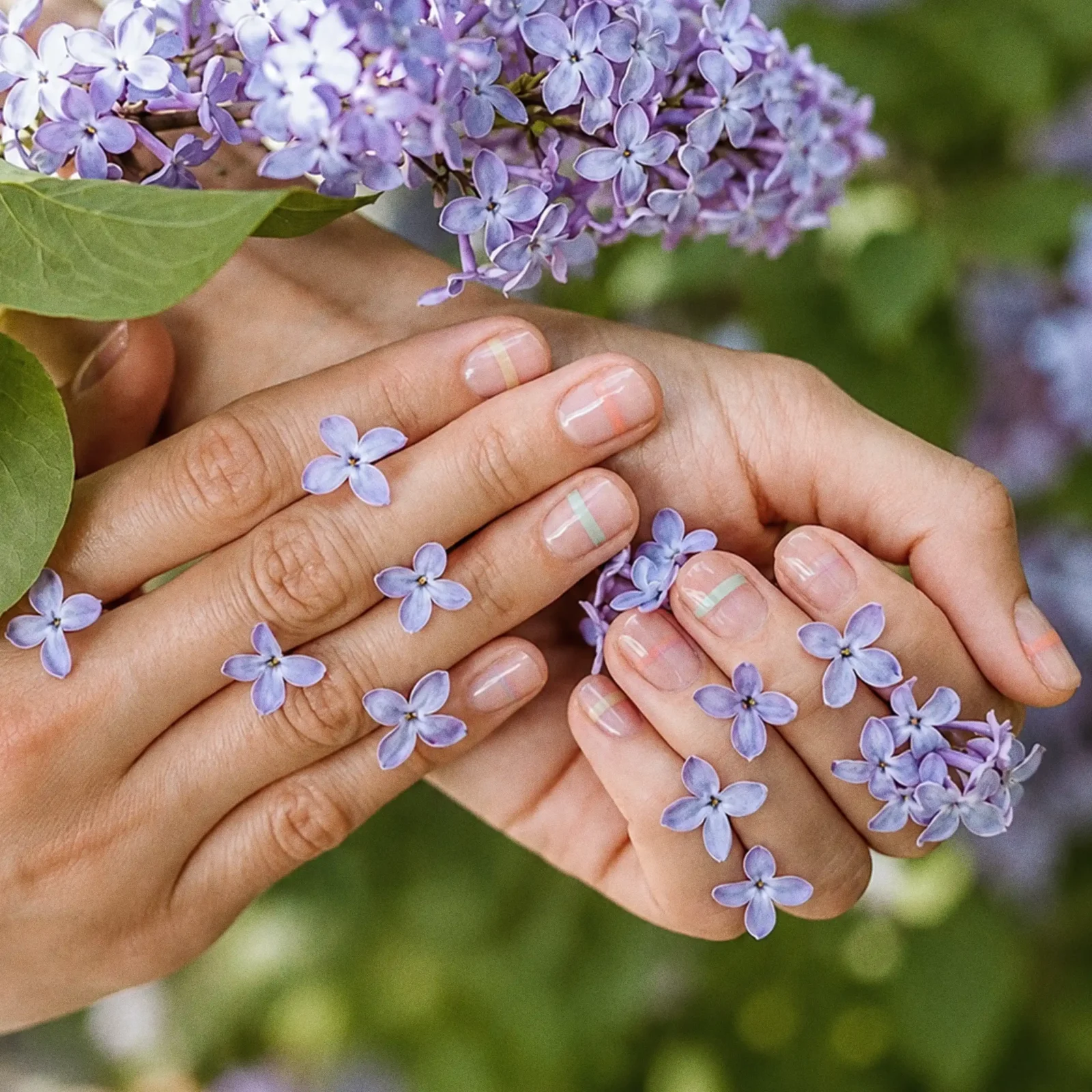 Close-up of a person holding a cluster of light purple lilac flowers with pastel-nail hands.