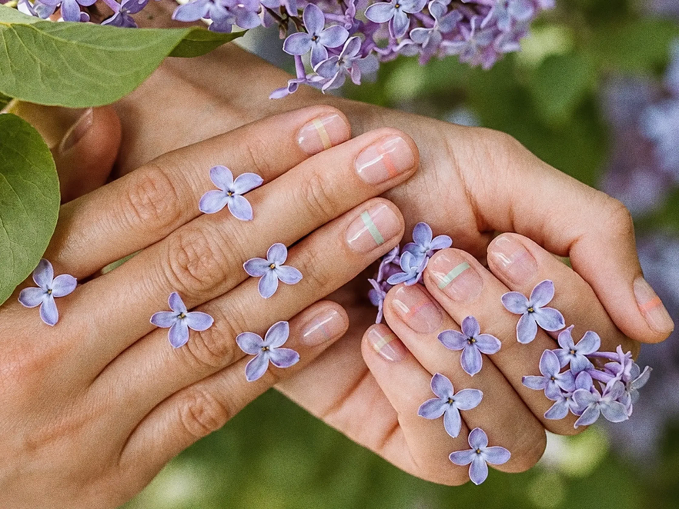 Hands holding light purple lilac blossoms with pastel striped nails