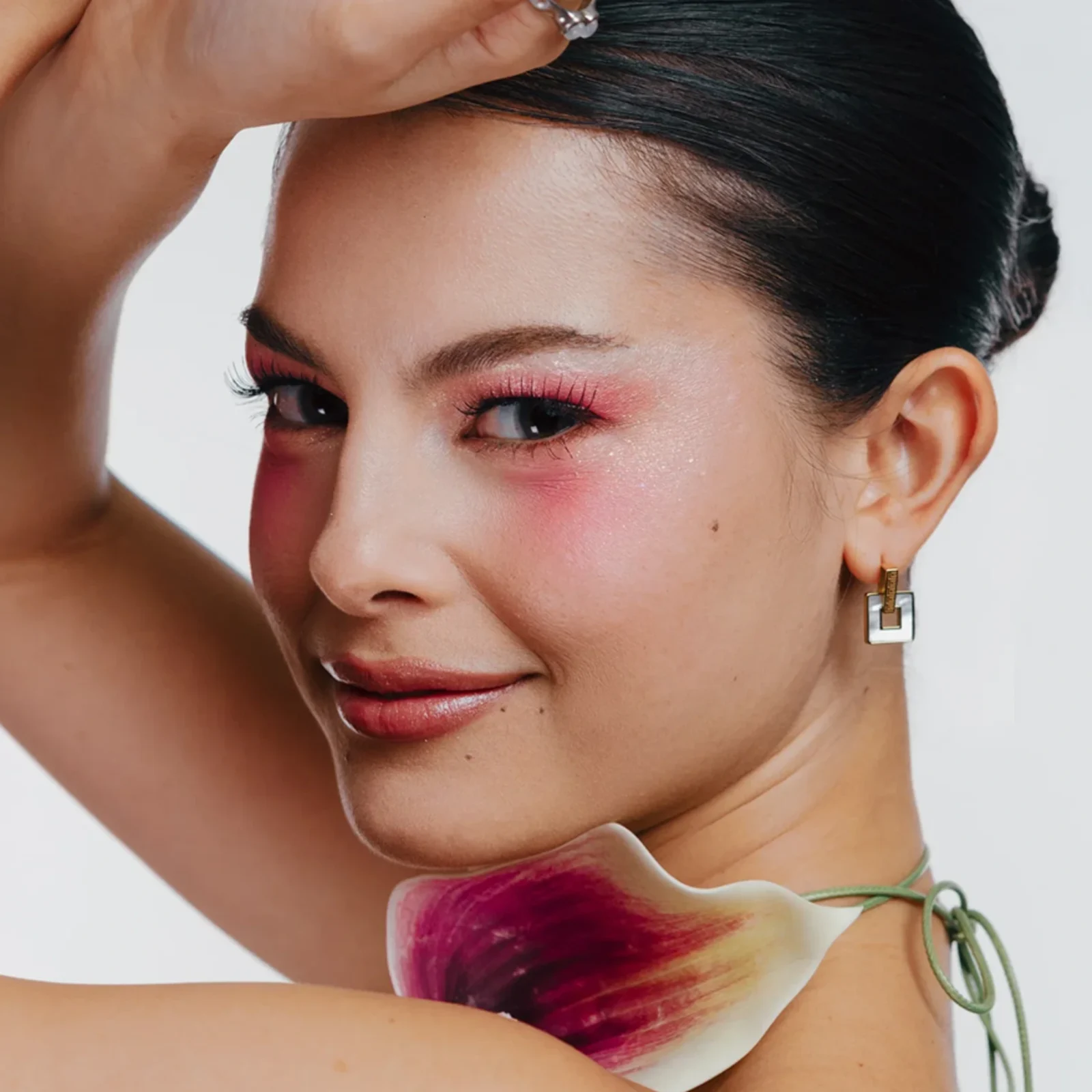 Close-up of a woman's lower face and neck with pink makeup, a floral scarf around the neck, and a hand resting on her head.