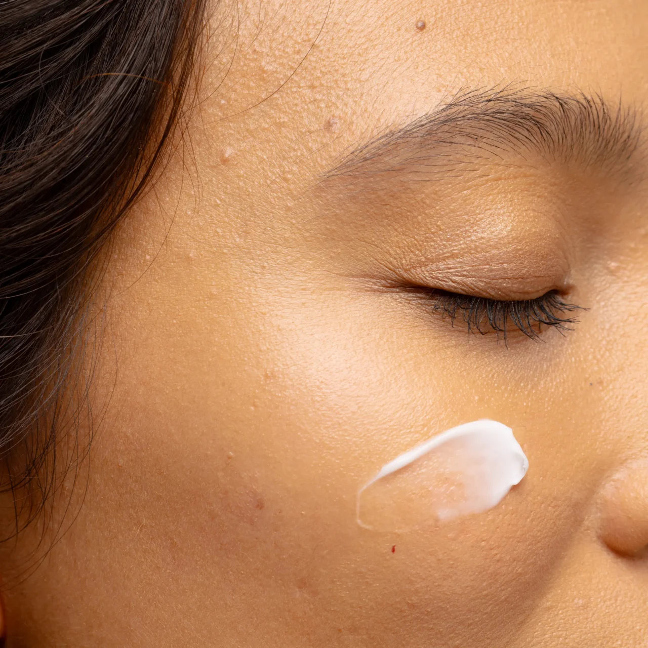 Close-up of the cheek area showing visible pores with a dab of white cream on the skin near the temple.