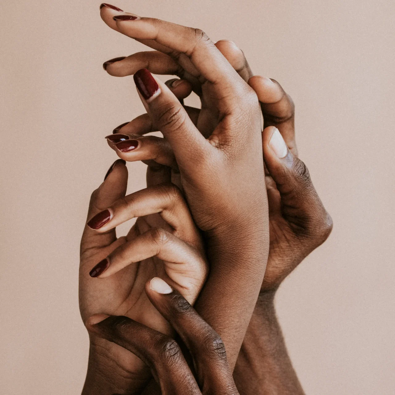 Interlaced hands of diverse skin tones against a beige background.