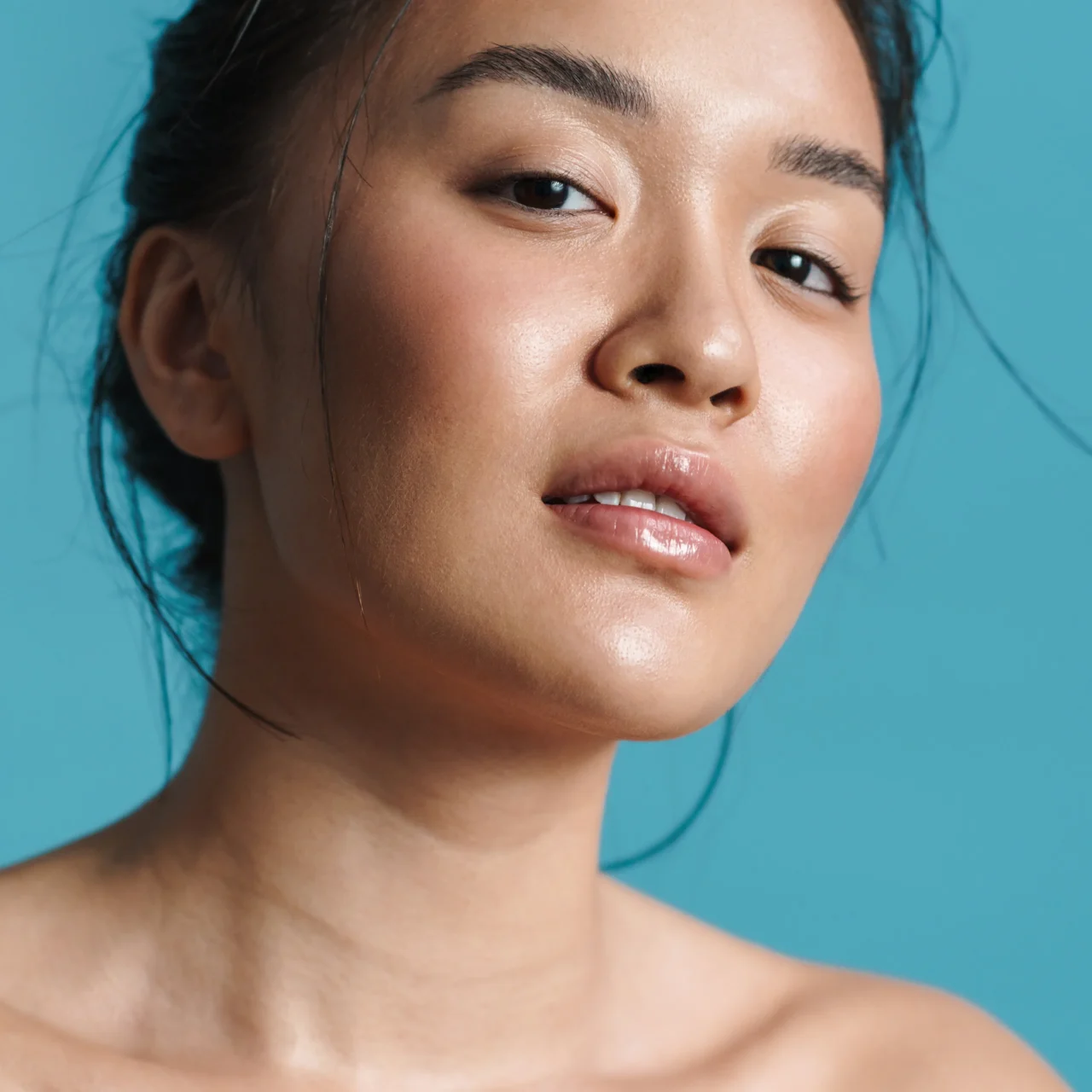 Close-up of a person's lips and chin with glossy skin against a turquoise background.