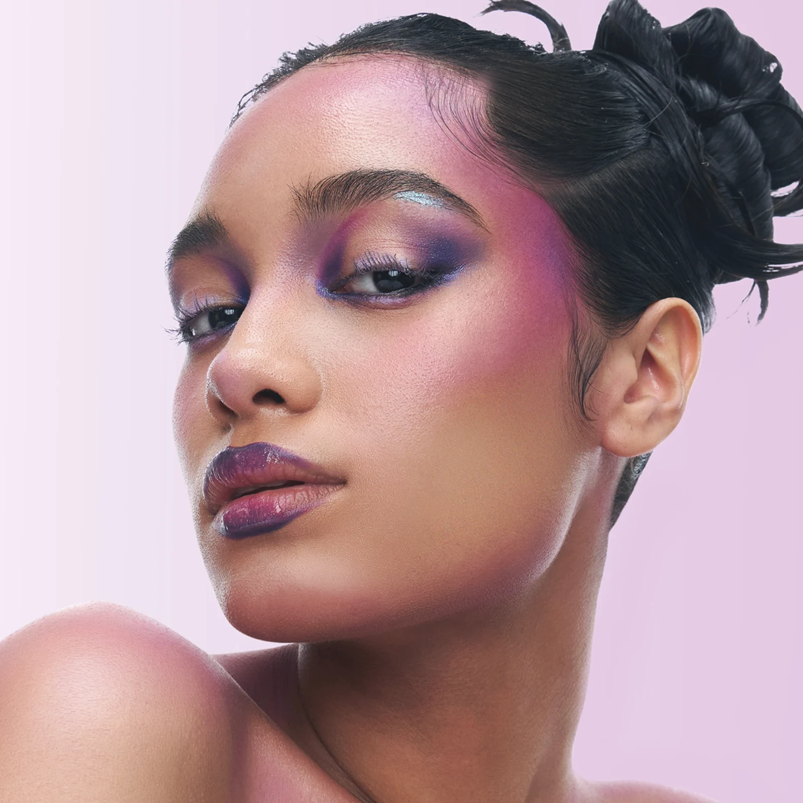 Close-up of a woman's face showcasing purple eyeshadow and pink lipstick against a pale pink background.