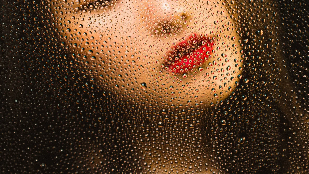 Close-up of red lips seen through a fogged glass covered in water droplets.