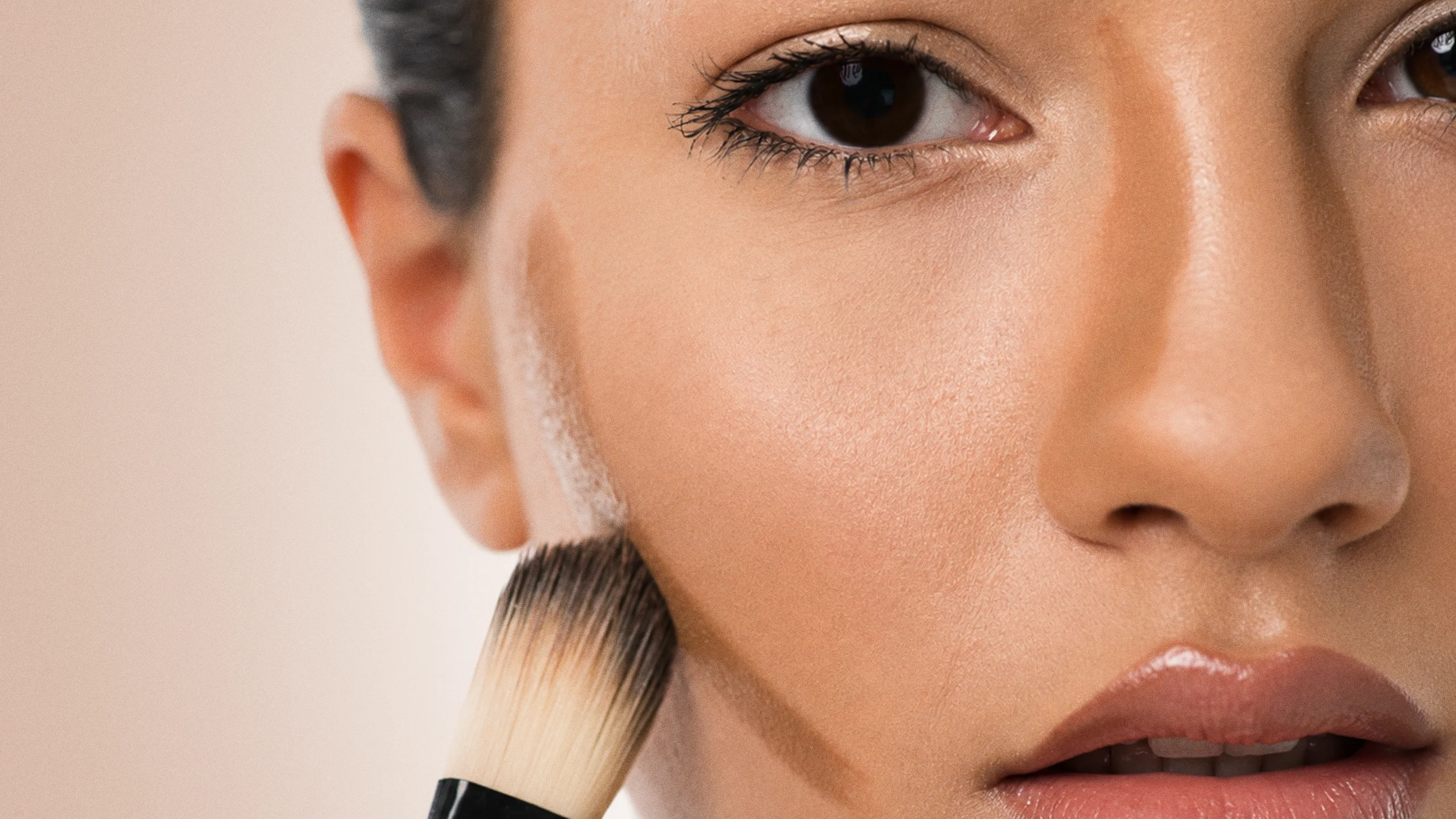 Close-up of a woman's face as a makeup brush applies foundation to her cheek.