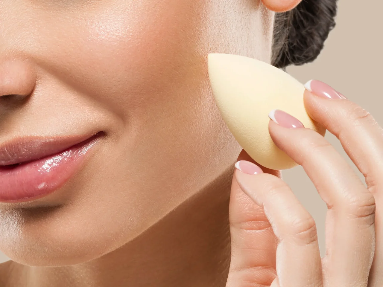 Close-up of a hand applying makeup foundation to a woman's cheek with a sponge.