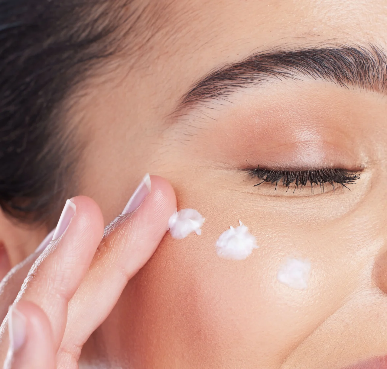 Close-up of a person near the eye, using cotton to apply or remove makeup along the lower eyelid and eyebrow area.